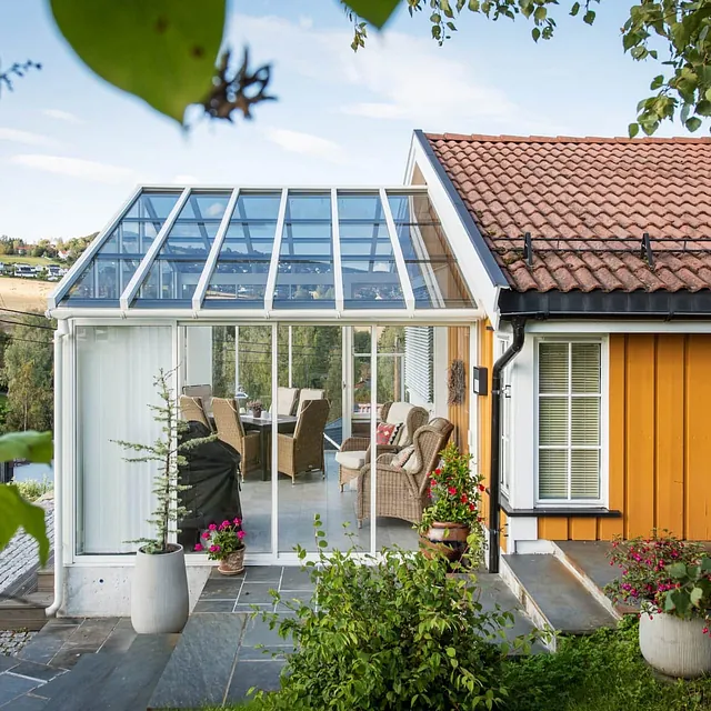 Lys utestue med glasstak og inngang fra hage