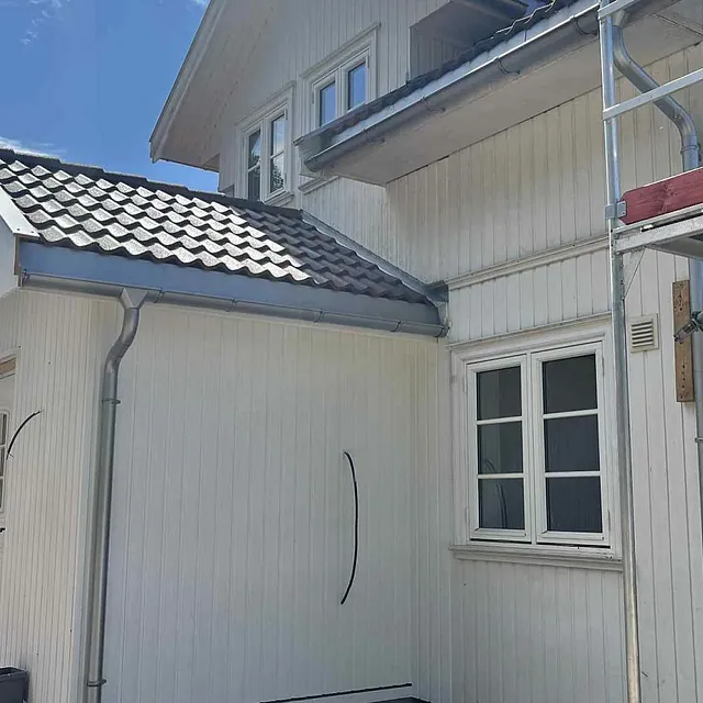 Hvit enebolig med nytt tilbygg og stillas på siden under oppussing i sollys.